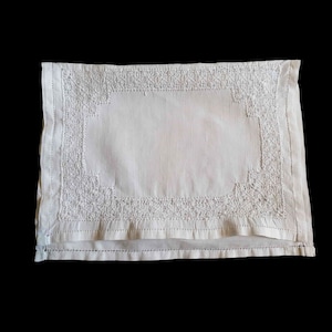May include: White linen placemat with a delicate embroidered border.