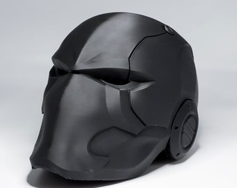 May include: A black plastic helmet with a detailed design, featuring a pointed chin guard and a textured surface.