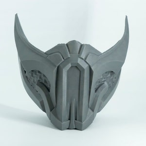 May include: A gray 3D printed mask with a geometric design and sharp points. The mask has a detailed pattern on the sides and a central ridge.