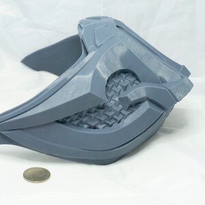 May include: A gray 3D printed mask with a geometric design. The mask is made of plastic and has a textured surface.