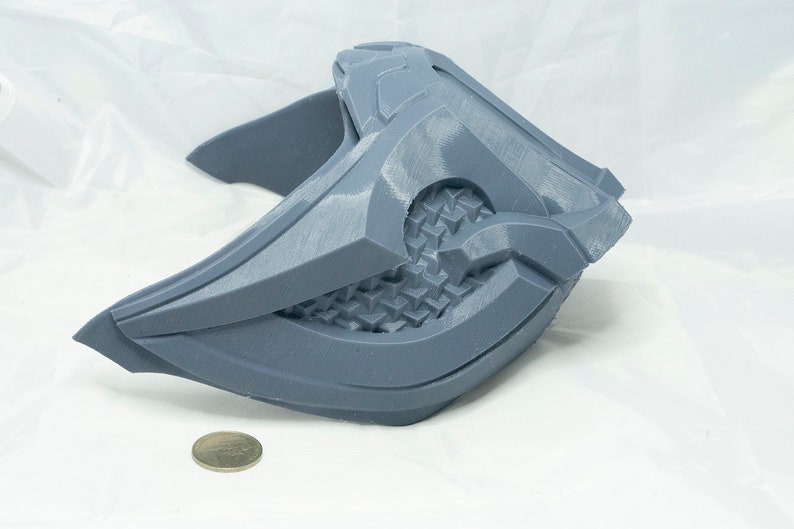 May include: A gray 3D printed mask with a geometric design. The mask is made of plastic and has a textured surface.