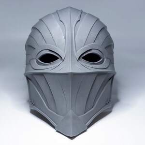 May include: A gray, detailed, helmet-like mask with eye holes and a pointed chin.