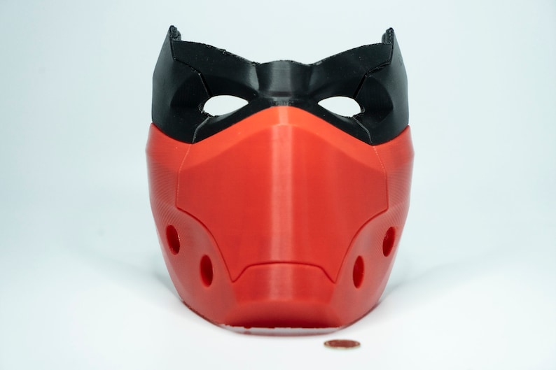 Peut inclure: Un masque imprim&eacute; en 3D rouge et noir avec des trous pour les yeux et le nez. Le masque a une surface textur&eacute;e et est con&ccedil;u pour couvrir le nez et la bouche.