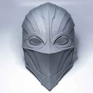 May include: A gray, detailed, 3D printed mask with a sharp, angular design. The mask has two eye holes and a pointed chin.