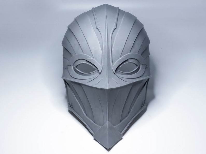 May include: A gray, detailed, 3D printed mask with a sharp, angular design. The mask has two eye holes and a pointed chin.