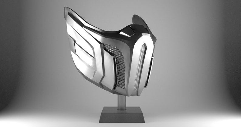 May include: A silver-colored mask with a geometric design. The mask is on a black stand.