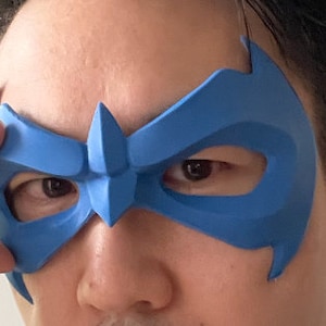 Peut inclure: Un masque en plastique bleu avec un design pointu au-dessus des yeux. Le masque est port&eacute; par une personne.