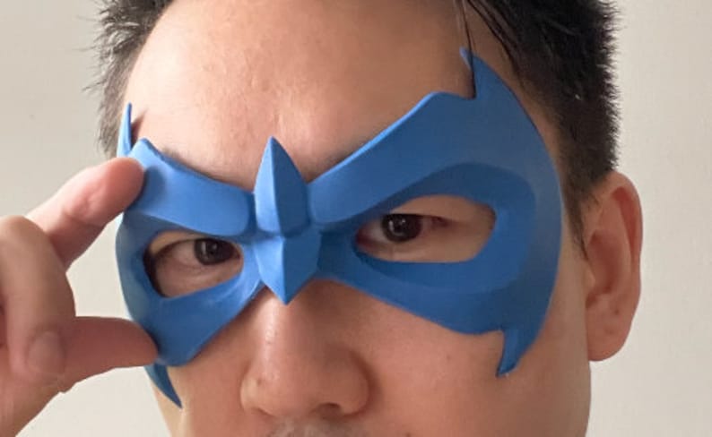 Peut inclure: Un masque en plastique bleu avec un design pointu au-dessus des yeux. Le masque est port&eacute; par une personne.