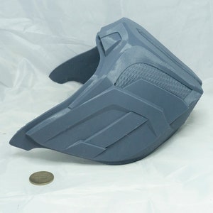 May include: A gray plastic mask with a textured surface and geometric designs. The mask is shaped like a half-face mask and has a curved shape.