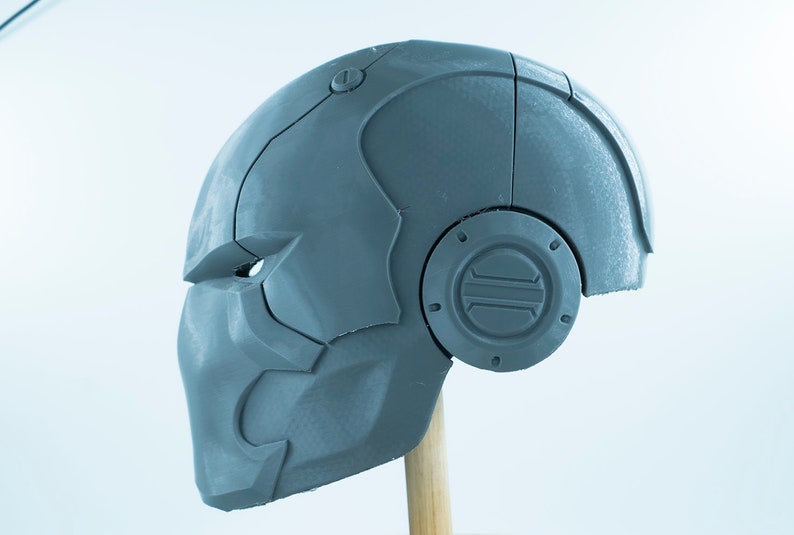 May include: A gray 3D printed helmet with a detailed design and a circular panel on the side.