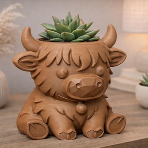 May include: A brown, Highland cow-shaped planter with a succulent plant. The planter has a detailed design, including horns, ears, and a bell. The succulent has green leaves. The planter is sitting on a wooden surface.