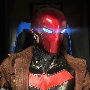 May include: A red and black superhero costume with a red helmet featuring a blue visor. The costume is worn over a brown leather jacket.