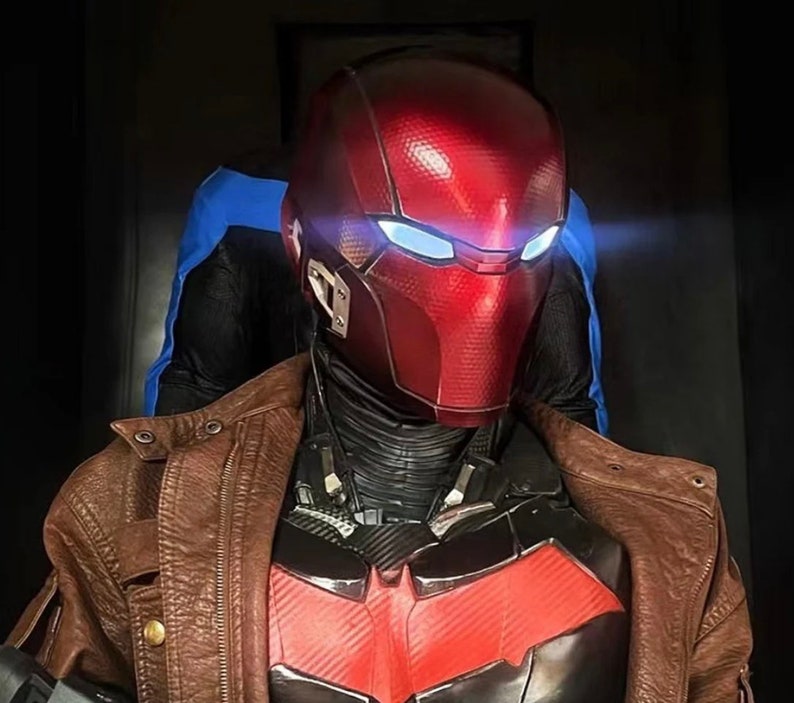 May include: A red and black superhero costume with a red helmet featuring a blue visor. The costume is worn over a brown leather jacket.
