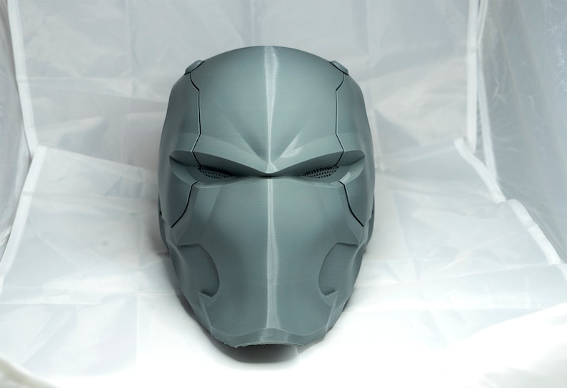 May include: A gray, 3D printed helmet with a futuristic design. The helmet has a visor and a detailed faceplate.