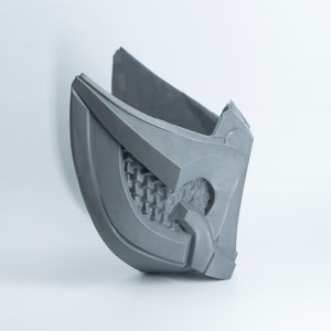 May include: A gray 3D printed mask with a detailed design. The mask has a geometric pattern and a raised edge around the eye area.