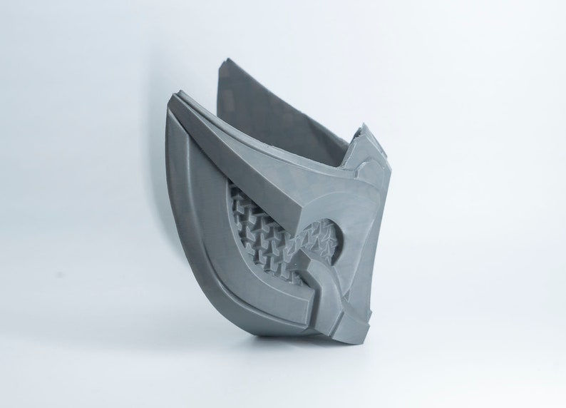 May include: A gray 3D printed mask with a detailed design. The mask has a geometric pattern and a raised edge around the eye area.