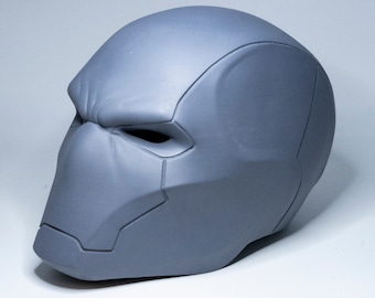 May include: A grey, unpainted, plastic Red Hood mask. The mask has a detailed design with a raised brow, a defined nose, and a sculpted chin.