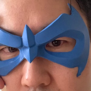 Peut inclure: Un masque de super-h&eacute;ros bleu avec un design pointu au-dessus des yeux. Le masque est fait d'un mat&eacute;riau lisse, semblable au plastique.