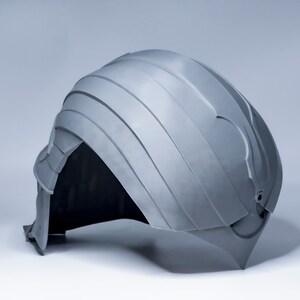 May include: A gray plastic helmet with a textured surface and a raised design on the top. The helmet has a small hole on the back.