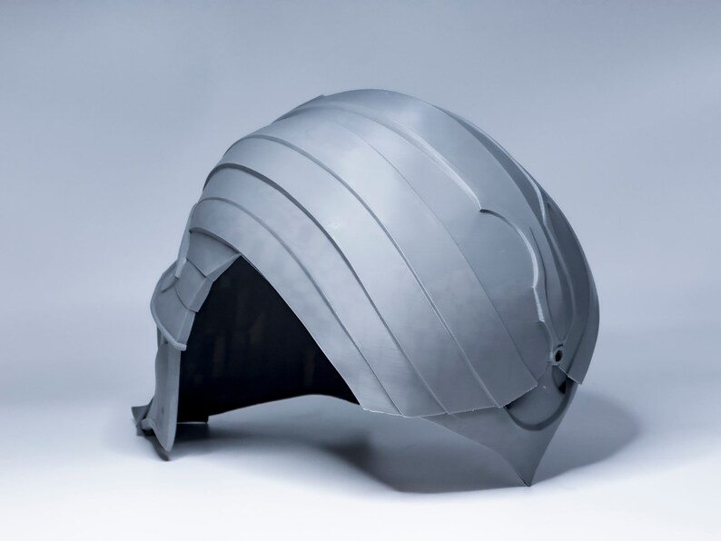 May include: A gray plastic helmet with a textured surface and a raised design on the top. The helmet has a small hole on the back.