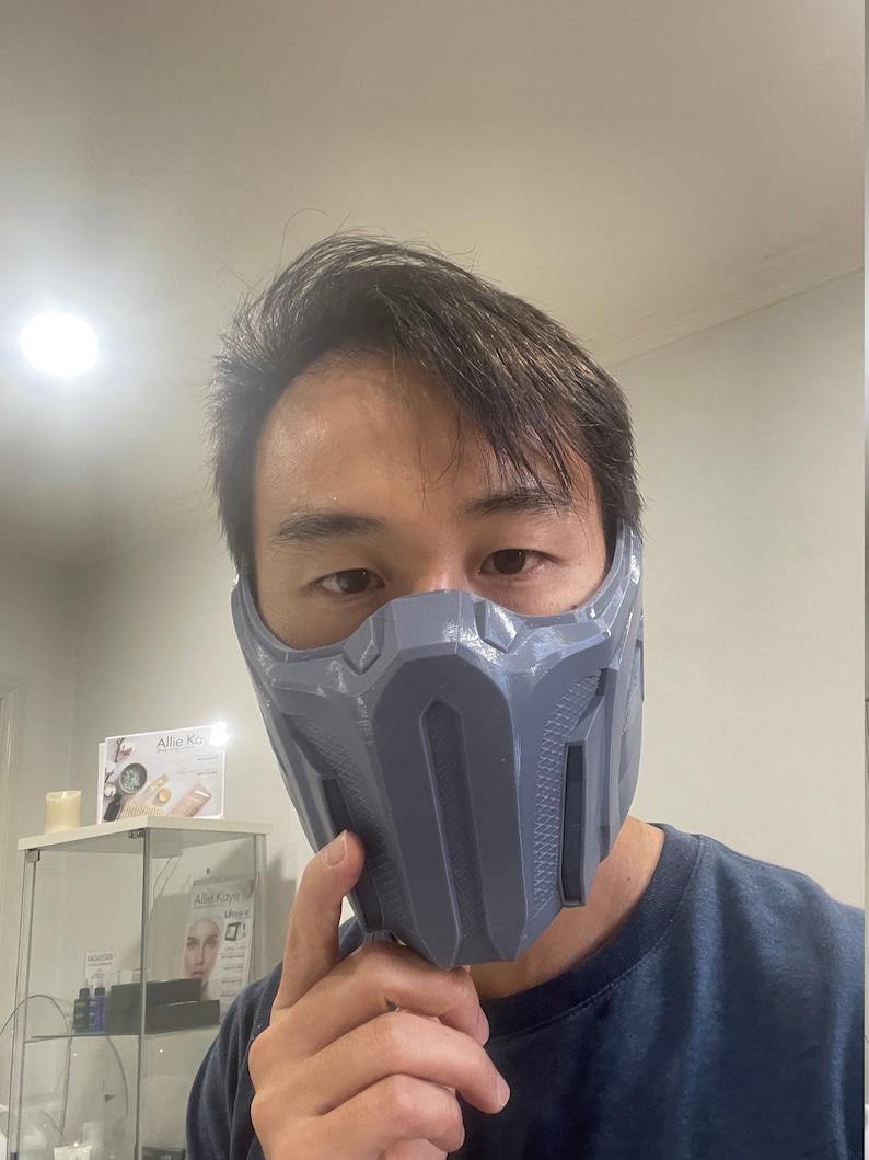 May include: A person wearing a gray, 3D printed mask that covers the nose and mouth. The mask has a geometric design with raised lines and a textured surface.