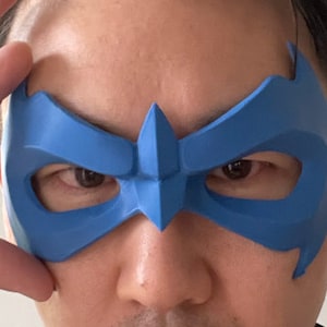Peut inclure: Un masque en plastique bleu avec un nez pointu et des trous pour les yeux. Le masque est port&eacute; par une personne, couvrant ses yeux et son nez.