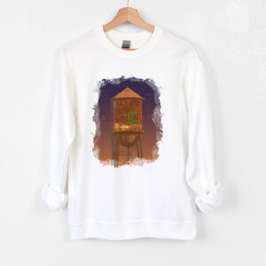 May include: White sweatshirt with a watercolor illustration of a rusty water tower with the words "Welcome to Nowhere" written on it.