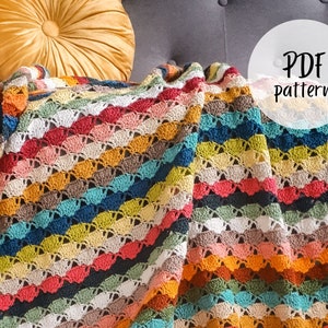 Op de afbeelding: Een kleurrijk gehaakt deken met een gestreept patroon in tinten rood, oranje, geel, groen, blauw en bruin. Het deken is gedrapeerd over een grijze bank met een geel kussen. De tekst "PDF Pattern" is in wit op een witte cirkel geschreven.