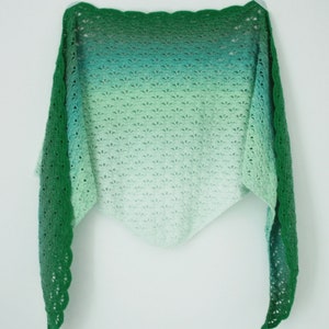 May include: A green and white crocheted shawl with a scalloped edge. The shawl is made with a gradient yarn that transitions from dark green to light green.