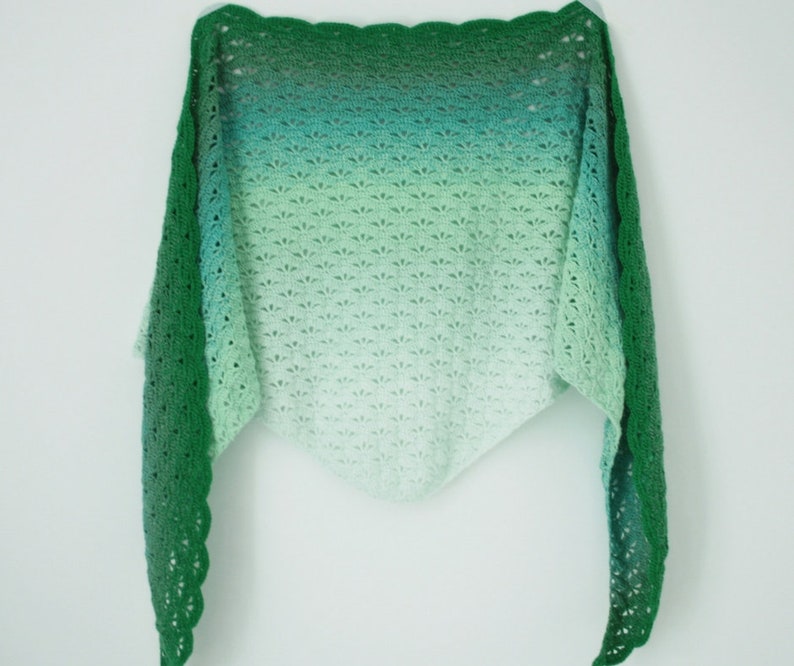 May include: A green and white crocheted shawl with a scalloped edge. The shawl is made with a gradient yarn that transitions from dark green to light green.