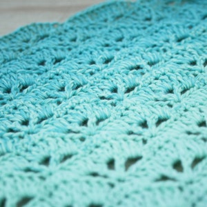May include: A close-up of a crocheted blanket with a gradient of blue and turquoise colors. The blanket is made with a delicate stitch pattern and has a soft, textured surface.