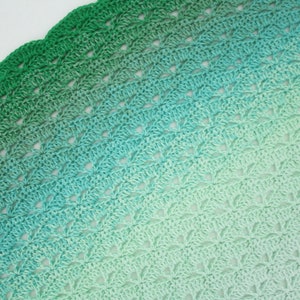May include: A crocheted blanket with a gradient of green and blue colors. The blanket is made with a delicate stitch pattern and has a scalloped edge.