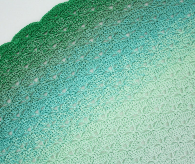 May include: A crocheted blanket with a gradient of green and blue colors. The blanket is made with a delicate stitch pattern and has a scalloped edge.