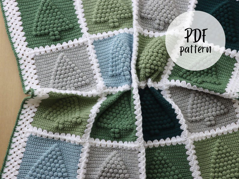 May include: A crochet blanket featuring a repeating pattern of green, grey, and blue squares. Each square has a textured, raised design resembling a Christmas tree. The blanket is edged with a white crochet border. The text "PDF Pattern" is written in white on a white circle in the top right corner of the image.