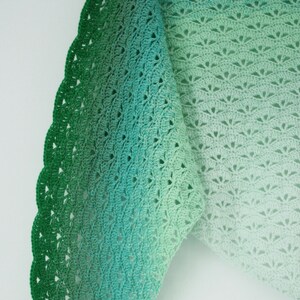 May include: A green crochet shawl with a gradient of color from dark green to light green. The shawl has a scalloped edge and a delicate openwork pattern.