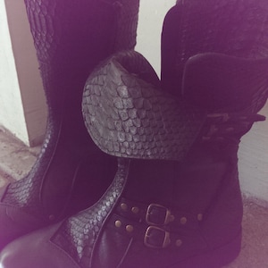 Puede incluir: Un par de botas de cuero negro con hebillas y un patrón de piel de serpiente. Las botas tienen un tacón grueso y una punta redonda.