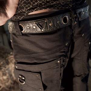 May include: Black cargo shorts with a black leather belt with metal accents. The belt has a large metal ring and rivets. The shorts have multiple pockets and a zipper detail.