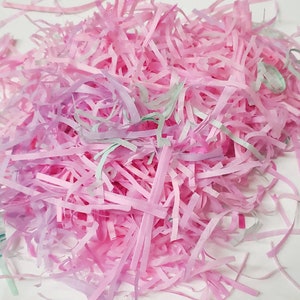 May include: A pile of pink and green shredded paper. The paper is in long, thin strips and is perfect for filling gift baskets or boxes.