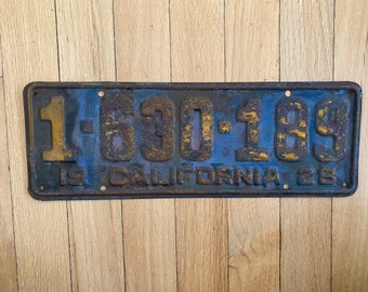 May include: A vintage blue and yellow California license plate with the number 1-630-189. The plate is rusty and has a faded blue paint finish.