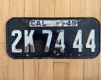 May include: Black California license plate with white lettering. The plate reads "CAL 45 2K 74 44".