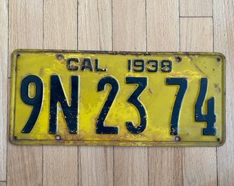 May include: A yellow metal license plate with black lettering. The plate reads "CAL 1938 9N 2374".