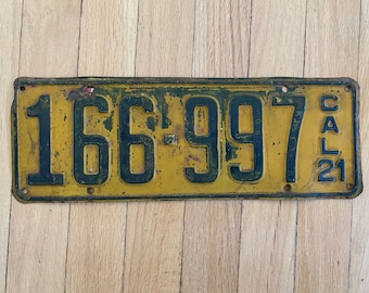May include: A yellow metal license plate with black numbers and letters. The plate reads "166-997 CAL 21".