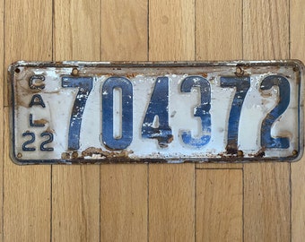 May include: A white metal license plate with blue numbers and letters. The plate reads "CAL 22 704372".