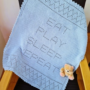 May include: A light blue crocheted baby blanket with a scalloped edge. The blanket has a repeating pattern of squares and is folded on a black chair.