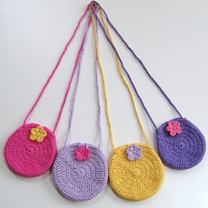 May include: Three crocheted purses with flower accents. The purses are pink, purple, and yellow. Each purse has a long strap.