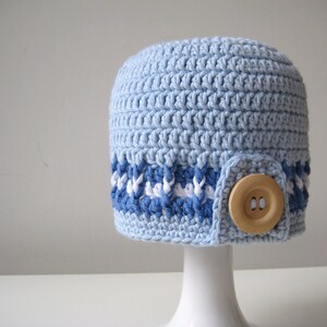 Puede incluir: Un gorro de punto azul claro con una banda a rayas blancas y azules y un bot&oacute;n de madera.