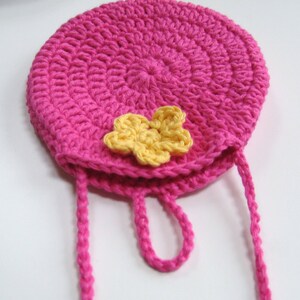 May include: A pink crocheted bag with a yellow flower accent and a long pink strap.
