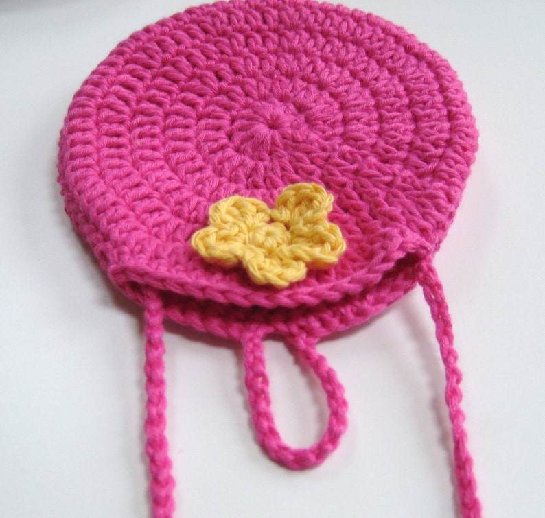 May include: A pink crocheted bag with a yellow flower accent and a long pink strap.