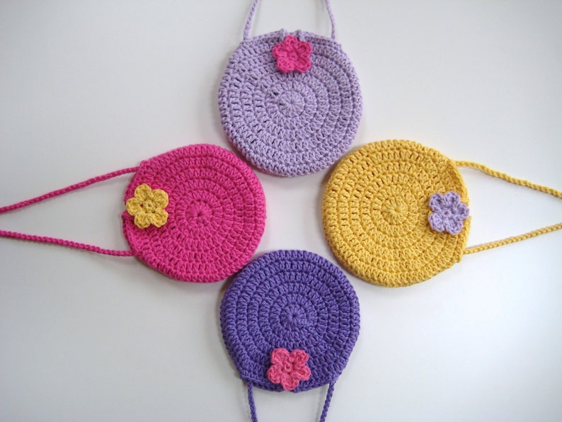 May include: Four crocheted purses with flower embellishments. The purses are in shades of purple, pink, and yellow.