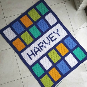 May include: A blue, white, green, and orange crocheted blanket with the name "HARVEY" spelled out in white yarn.
